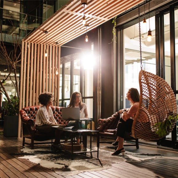 Three women sitting in a modern office lounge with decorative wooden shading and hanging egg chair
