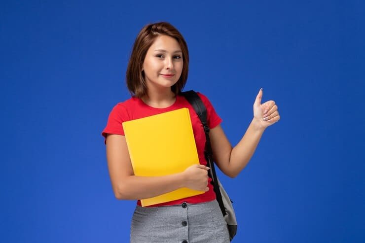 A confident female student holding a yellow file and giving a thumbs up, representing successful tuition services in Karachi.