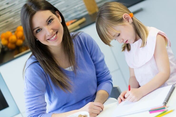 A smiling mother or female tutor assisting a young child with drawing and creative learning at home in Karachi.