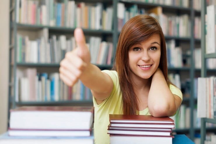 A smiling female student giving a thumbs up in a library, representing academic success with Expert Tutors Karachi.